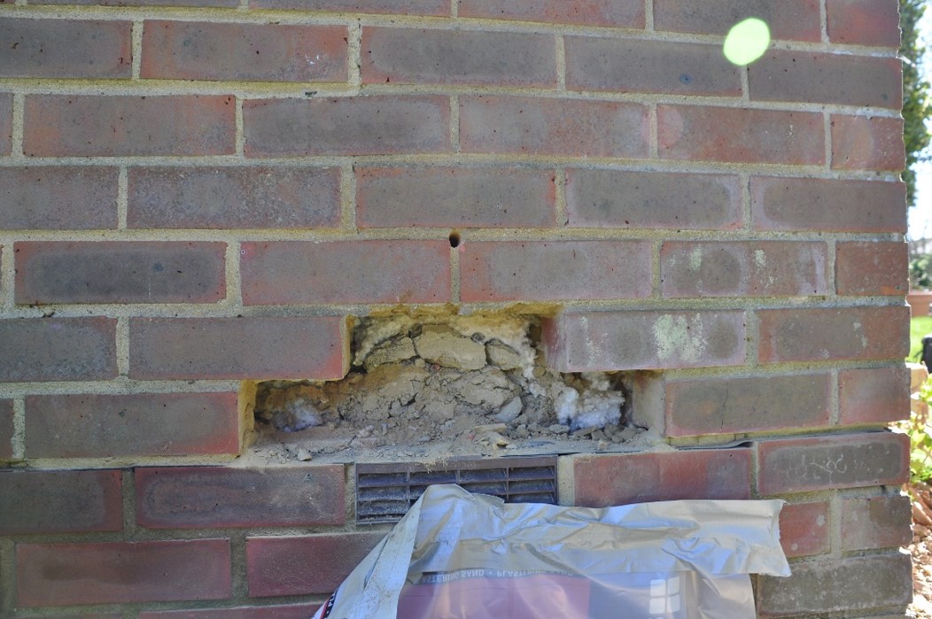 A photograph of a red brick wall with three bricks removed from it, revealing rubble behind.
