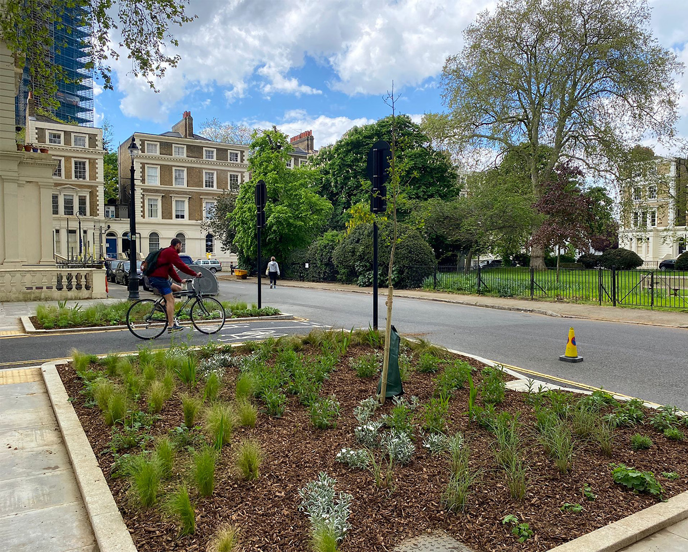 Person cycling between flower beds near houses