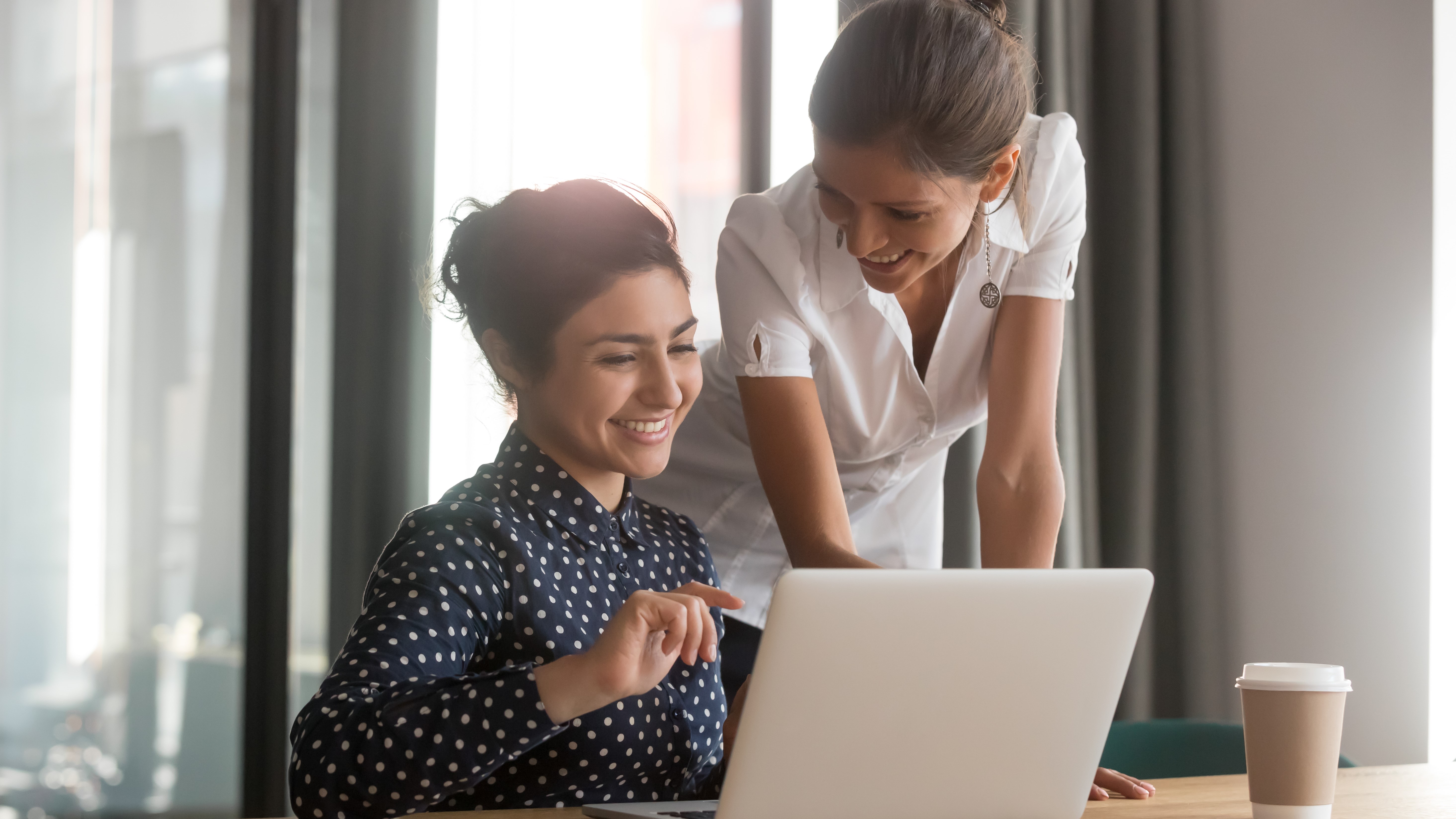 Young Asian woman sitting next to older standing white woman