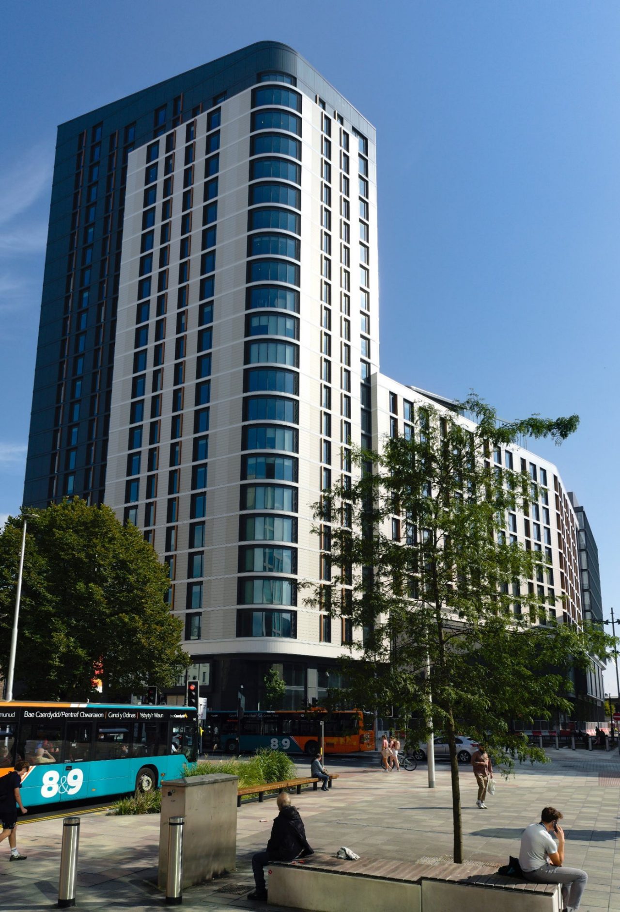 Image of tall building with trees and buses surrounding the facade.